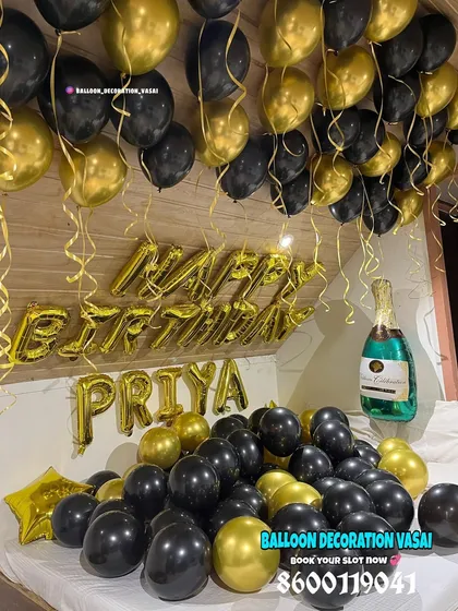A chic and stylish birthday room setup using a black and gold color scheme. The bed is filled with balloons, and the wall features "Happy Birthday" and a personalized name in gold foil letters.