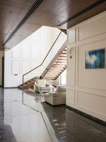 A wider view of the Triveni Farmhouse interior, showing the polished marble floors reflecting the light and the elegant interplay between the modern staircase and classic wall details.