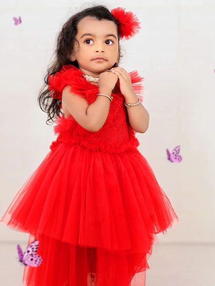 A girl in a vibrant red dress stands among purple butterfly decorations. The simple white background allows her personality and colorful outfit to take center stage.