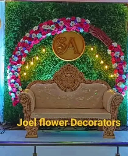 This modern engagement stage features a lush greenery wall with a circular floral arch and a custom 'SA' monogram. Hanging lanterns and spotlights add a warm, celebratory glow to the event.