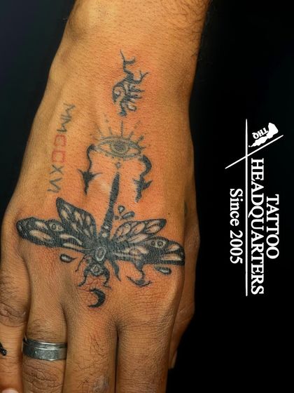 A hand tattoo featuring a large dragonfly, an all-seeing eye, and other mystical symbols.