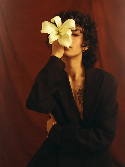 A conceptual portrait where a white lily hides the model's face. This image plays with themes of beauty, identity, and nature in the context of men's fashion.