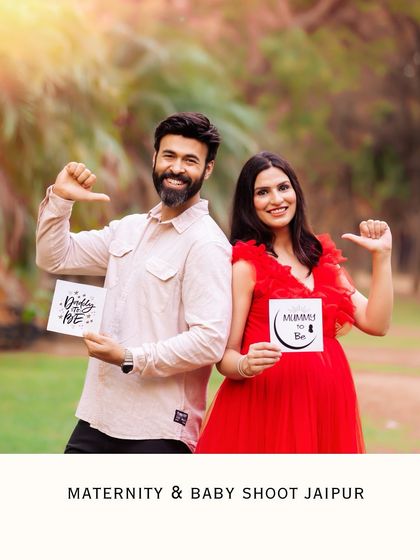 A fun outdoor announcement photo. The couple stands back-to-back, holding signs that say "Daddy to be" and "Mummy to be," sharing their exciting news with a smile.