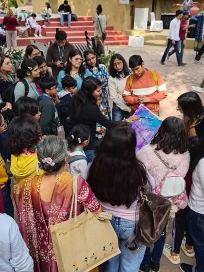 An instructor provides feedback and guidance to a group of students, who gather around to see the progress on a colorful painting.