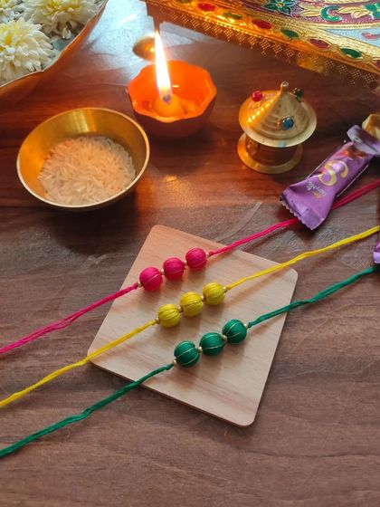 A set of colorful thread-bead rakhis. These are available in bright pink, yellow, and green, perfect for a festive celebration.