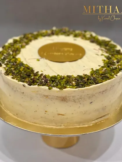 A simple and elegant anniversary cake. The cake is frosted with a light pistachio cream and generously topped with crushed pistachios, finished with a gold "Happy Anniversary" plaque.