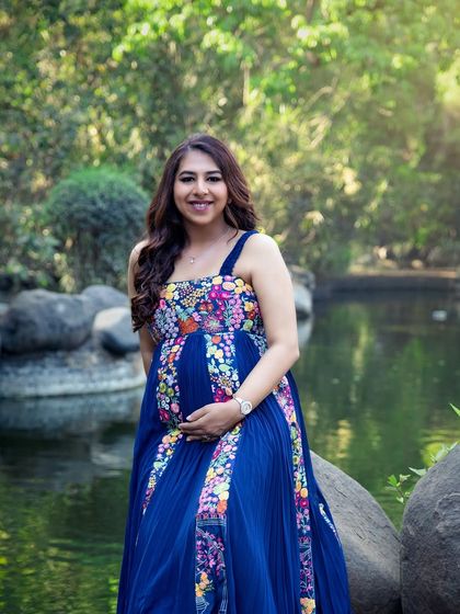 A vibrant solo portrait by the water in a beautiful park. The floral dress complements the natural surroundings perfectly, creating a stunning and colourful maternity photo.