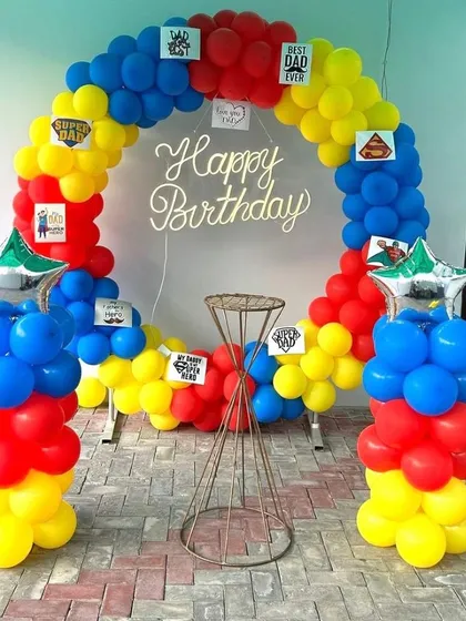 A fun balloon arch decoration for a father's birthday. The primary colors of red, yellow, and blue are accented with 'Best Dad' and 'Super Dad' cards, making it a personalized and cheerful setup.