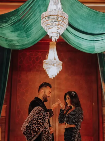 The couple shares a delicate, intimate moment under a grand crystal chandelier, a perfect blend of romance and opulent decor during their reception.