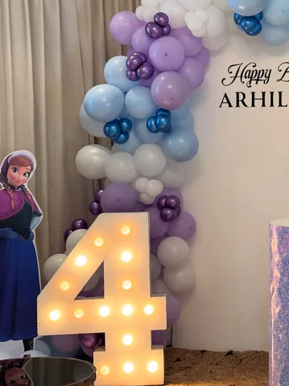 Anna stands by the glowing number '4' marquee light, part of the enchanting Frozen birthday setup.
