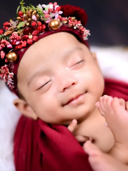 A close-up of a sleeping newborn with a beautiful floral headband. The focus is on their peaceful expression and delicate features.