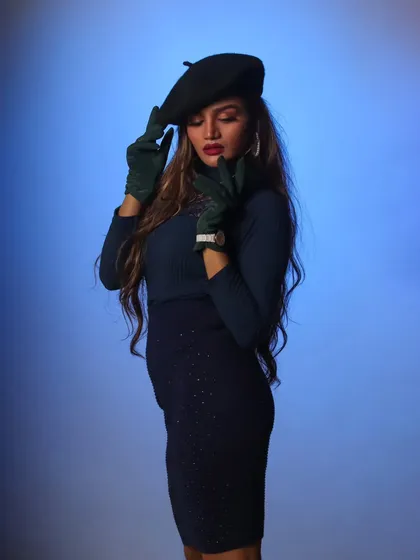 A chic, stylized portrait of a model wearing a beret and gloves. The blue background and pose give it a high-fashion, editorial feel.