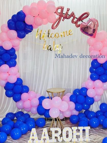 A "Welcome Baby Girl" decoration with a circular balloon arch in vibrant blue and pink. Foil balloons spelling out the message are placed in the center, with the baby's name in letters at the base.