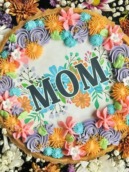 A close-up on the 'MOM' tart nestled within the colorful flowers, showcasing the intricate buttercream piping and thoughtful design.