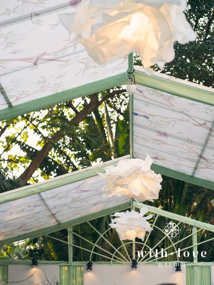 Custom paper flower light fixtures hanging from the ceiling of 'The Conservatory' tent, adding a whimsical and artistic touch.