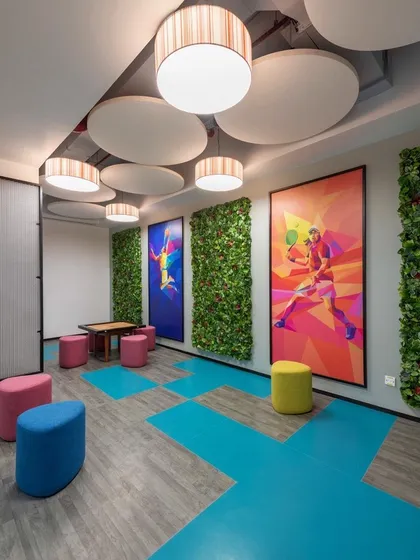 A games room with colorful poufs, vertical green walls, and large, vibrant sports-themed artwork. The flooring incorporates geometric patterns in blue and grey.