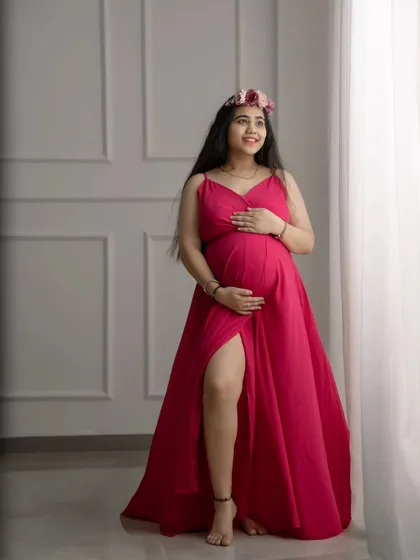 A vibrant and joyful solo portrait. The bright pink gown and floral crown add a pop of color against the clean, minimalist studio background.