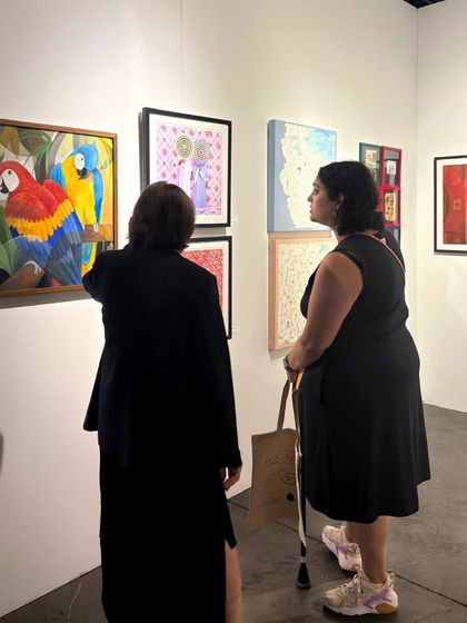 Two visitors closely observing a colorful painting of parrots by Senaka Senanayake at our Seattle booth. This moment captures the quiet contemplation and personal connection that art inspires.