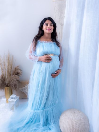 A peaceful and serene lifestyle portrait from our studio. The mom-to-be is wearing a light blue gown and looking thoughtfully out a window.
