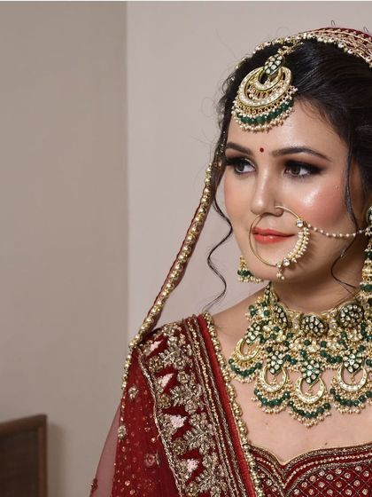 A side profile showcasing the intricate details of this maroon bridal lehenga and green Kundan jewellery set. The beaded dupatta adds another layer of elegance.