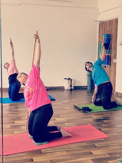 Students exploring a gentle side bend while kneeling, using the stick to guide the movement. This helps to stretch the side body and improve flexibility in the spine and shoulders.