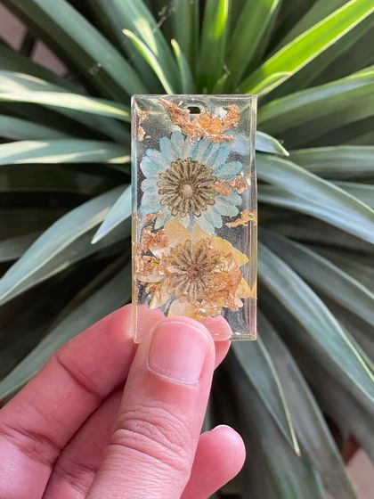 A close-up of a beautiful resin keychain made with dried flowers and gold flakes, a small but stunning creation.