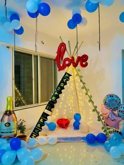 A cute and cozy birthday teepee setup. The tent is decorated with a 'Happy Birthday' banner and 'Love' foil balloon, perfect for an intimate celebration at home.