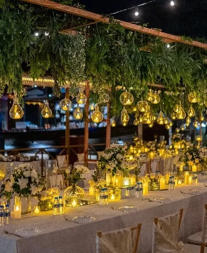 A wide shot of the candlelit dinner setup in Goa, with hanging glass orbs and lush greenery creating a magical overhead canopy.
