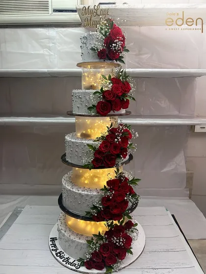 A towering statement of celebration. This multi-tiered cake with separators is illuminated from within and adorned with clusters of red roses, creating a truly spectacular display for a grand event.