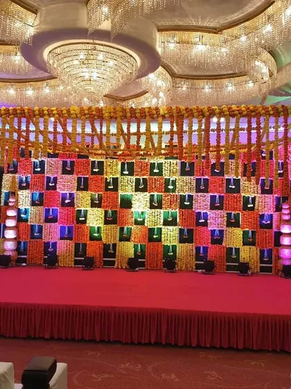 A vibrant and traditional Sangeet stage in a banquet hall. The backdrop features a colorful checkerboard pattern with marigold details, creating a perfect setting for musical performances.