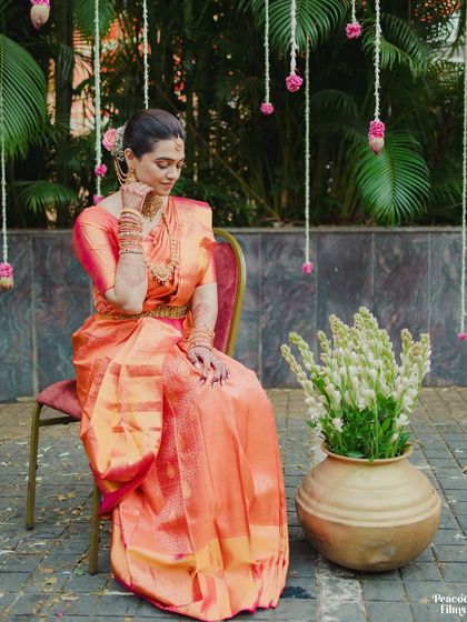 A seated portrait of the bride in a beautiful peach-colored silk saree, capturing a moment of quiet elegance.