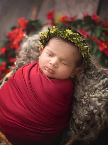 A bold and beautiful setup with a baby in a deep red wrap, nestled in a basket surrounded by flowers. This is a perfect look for a Valentine's or festive theme.