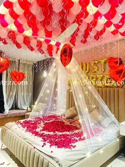 For a truly romantic first night or wedding surprise, I create setups like this one. It features a beautiful canopy over the bed with fairy lights, 'Just Married' foil balloons, and a ceiling full of red and white balloons. I also scatter fresh rose petals on the bed to complete the look.