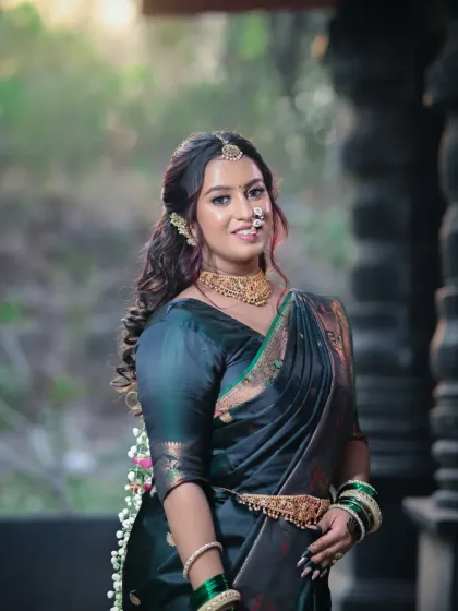 A smiling bride, confident and radiant in her dark green saree and traditional gold jewelry.