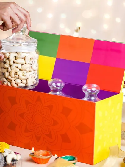 A vibrant and colorful Diwali hamper being opened to reveal jars of nuts. This action shot creates a sense of excitement and discovery, perfect for a gift unboxing theme.