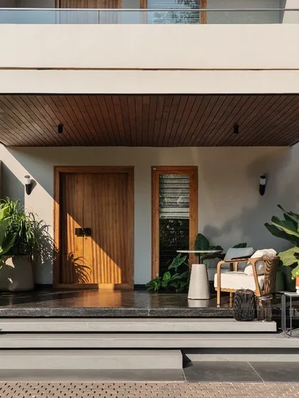 The entrance porch is designed as a welcoming transition space. A solid wood door, comfortable seating, and abundant greenery create a serene first impression before even stepping inside.