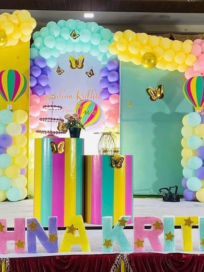 A vibrant and colorful butterfly and hot air balloon theme. The stage is decorated with multiple pastel balloon arches and rainbow-colored plinths, creating a cheerful and playful atmosphere.