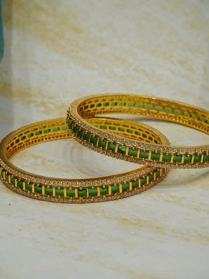 A pair of elegant bangles with green stones and a border of sparkling American diamonds. These are perfect for both traditional and contemporary outfits.