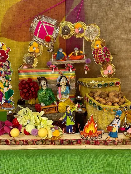 This hamper captures all the colorful vibes of Lohri. It features a decorated platter with figurines, a miniature swing, and jute bags filled with peanuts and other festive treats.