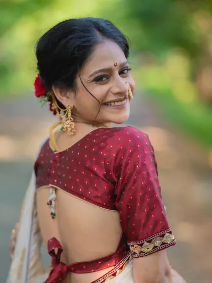 A happy bride showing off her beautiful backless blouse and floral bun. The makeup is minimal, letting her smile and the traditional attire be the focus.