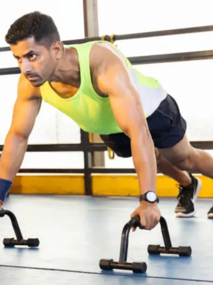 A client holding a push-up position on parallettes. This variation allows for a deeper range of motion and is great for chest and tricep development.