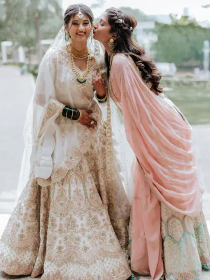 Such a sweet moment. The bride's soft, ethereal makeup in her white lehenga contrasts beautifully with her sister's fresh, rosy look.