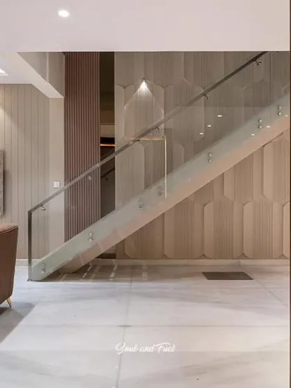 A glimpse into a modern living area, showing a sleek TV unit and a staircase with a glass railing. The neutral color palette and clean lines create a sophisticated and uncluttered atmosphere.