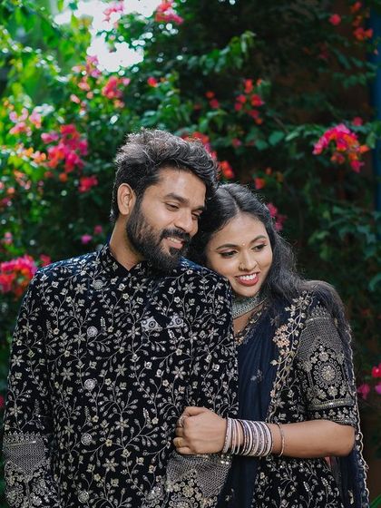 An intimate portrait of a couple in ornate traditional wear, surrounded by pink flowers.
