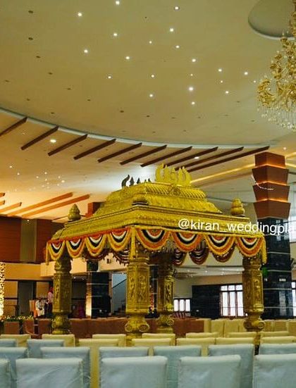 A wide view of a golden temple-style mandap set in the center of a large convention hall, showing how it becomes the focal point of the entire wedding.