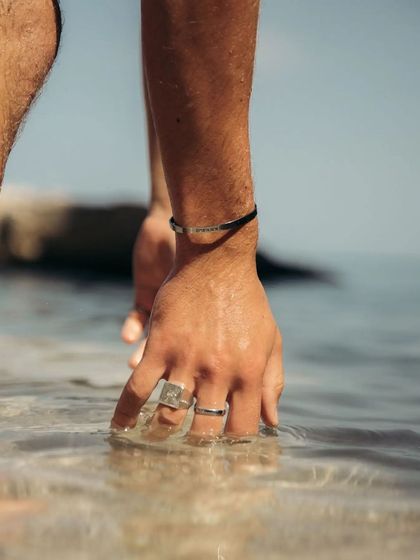 A man wearing a black cuff dips his hand into the water, demonstrating the bracelet's waterproof quality in a real-world setting.