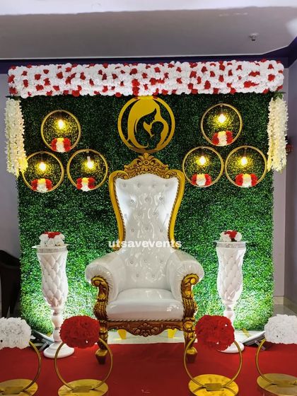 A simple baby shower backdrop with a green grass wall and hanging floral rings. The white throne chair and floral stands create a clean and elegant look.