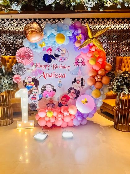 A fairy-themed first birthday with a photo collage backdrop, surrounded by a colorful balloon ring and fairy character cutouts.