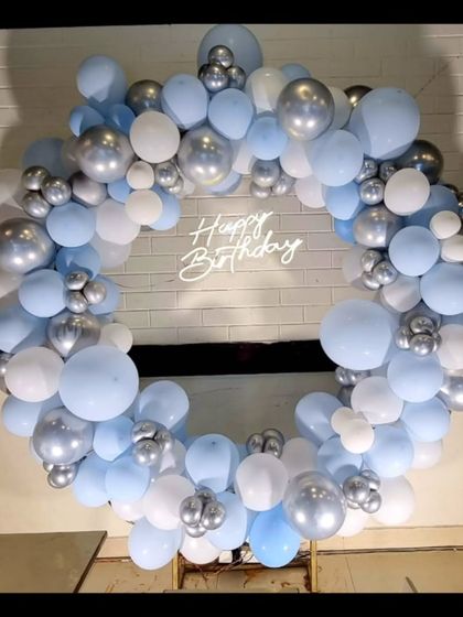 A beautiful and simple balloon ring in shades of baby blue, white, and silver with a 'Happy Birthday' neon sign.