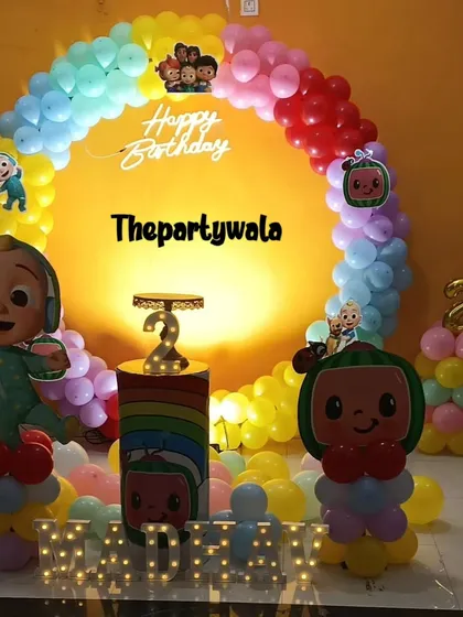A bright and cheerful Cocomelon theme against a yellow wall. The rainbow balloon arch and themed pedestal look fantastic and full of energy.